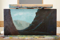 A landscape painting within a dark canyon opening looking out to a distant dessert hill.