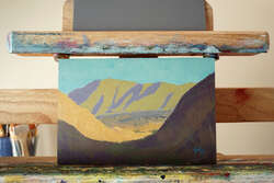 Painting of a desert landscape looking out at mountains across a sloping valley from a shaded morning canyon.