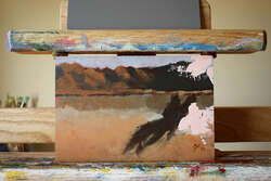 A vague painting of a desert scene. Mountains and sky in the distance reflect in a recently filled dry lake bed. A dark shape sprawls across the lower to mid-right. A smear of white intrudes from the right top.